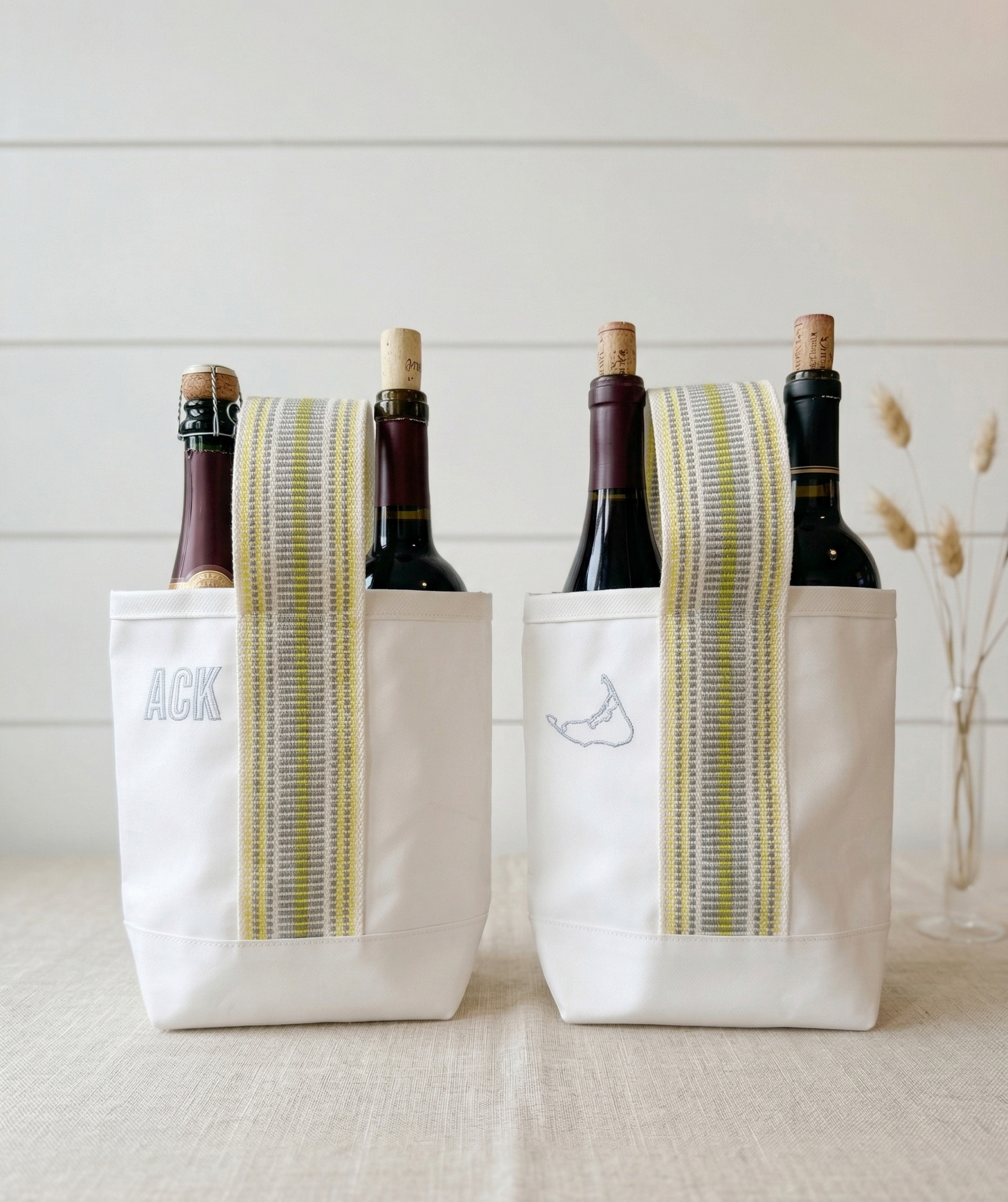 Two wine bottles in white bags with striped green and yellow bands on a light surface.