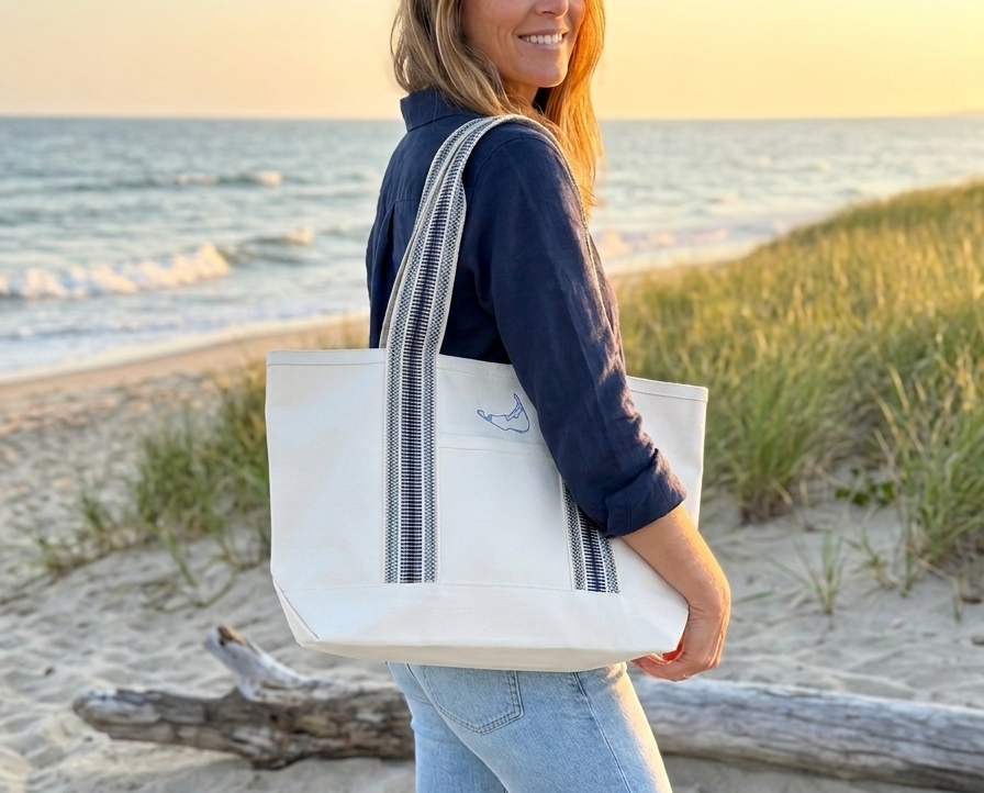 Woman holding a white tote bag with a logo on a beach at sunset